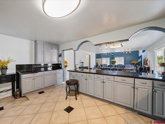 kitchen with track lighting, gray cabinetry, light tile flooring, and dark stone countertops