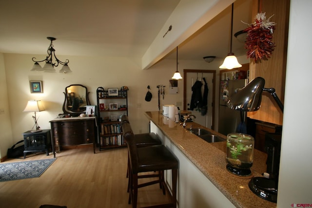 bar featuring light stone counters, sink, pendant lighting, and light hardwood / wood-style flooring