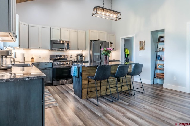 kitchen featuring sink, a center island, wood-type flooring, decorative light fixtures, and appliances with stainless steel finishes