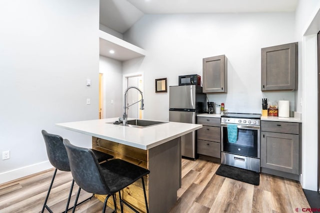 kitchen with a breakfast bar, sink, an island with sink, appliances with stainless steel finishes, and light hardwood / wood-style floors