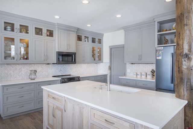 kitchen with decorative backsplash, appliances with stainless steel finishes, a kitchen island with sink, dark wood-type flooring, and sink