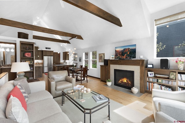 living room featuring beamed ceiling, high vaulted ceiling, light wood-type flooring, and a fireplace with flush hearth