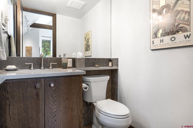 half bathroom featuring tile walls, toilet, and vanity