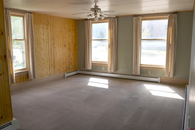 empty room with wood walls, ceiling fan, a baseboard radiator, and carpet flooring