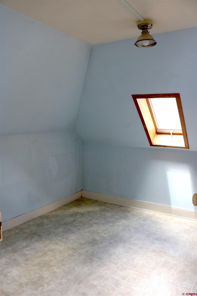 bonus room with light tile flooring and lofted ceiling with skylight