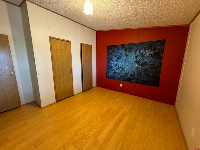 unfurnished bedroom featuring a textured ceiling, two closets, and light wood-type flooring