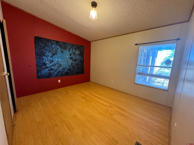 empty room featuring lofted ceiling, a textured ceiling, and light wood-type flooring