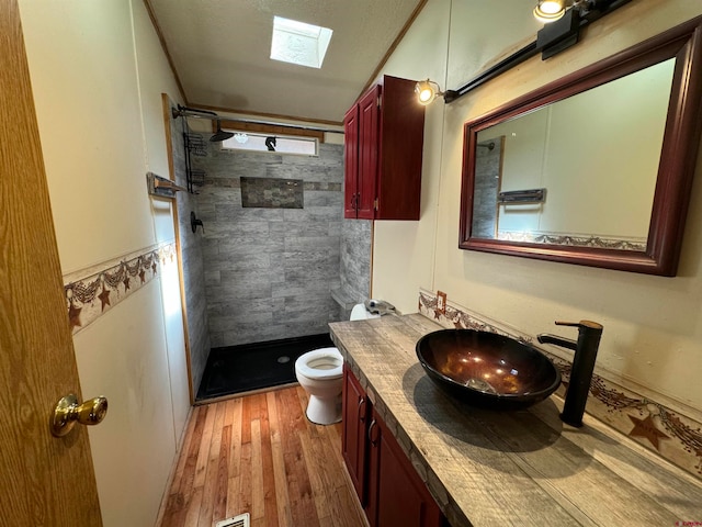 bathroom with a skylight, toilet, hardwood / wood-style flooring, a tile shower, and vanity