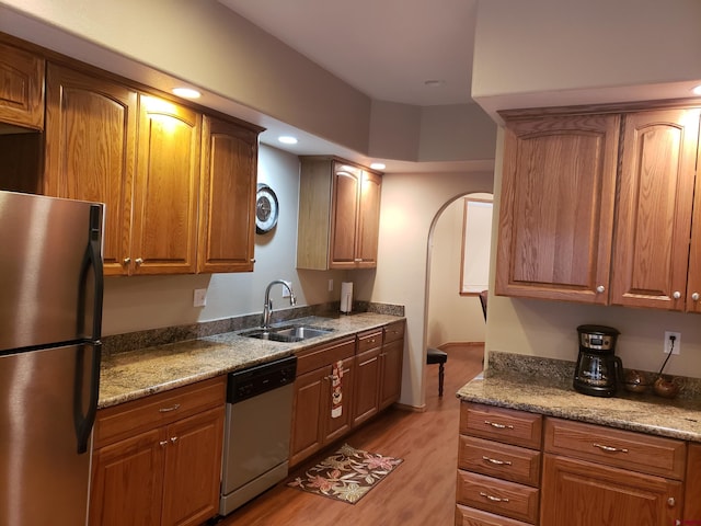 kitchen with stone counters, appliances with stainless steel finishes, light hardwood / wood-style floors, and sink