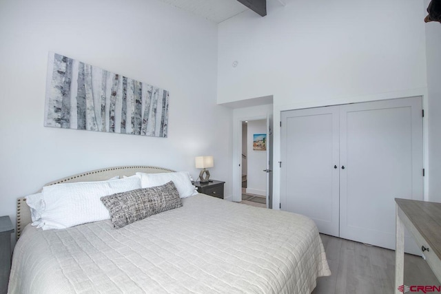 bedroom featuring beam ceiling, high vaulted ceiling, a closet, and light wood-type flooring