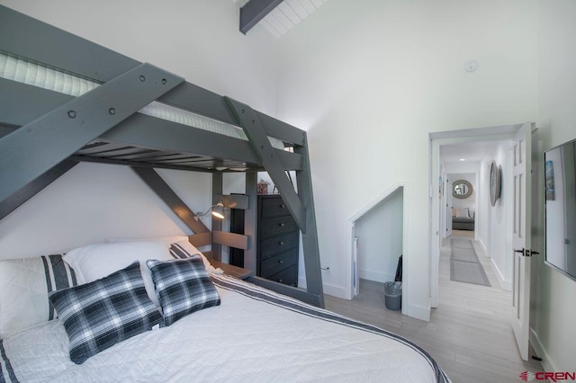 bedroom featuring beamed ceiling, a towering ceiling, and light hardwood / wood-style floors