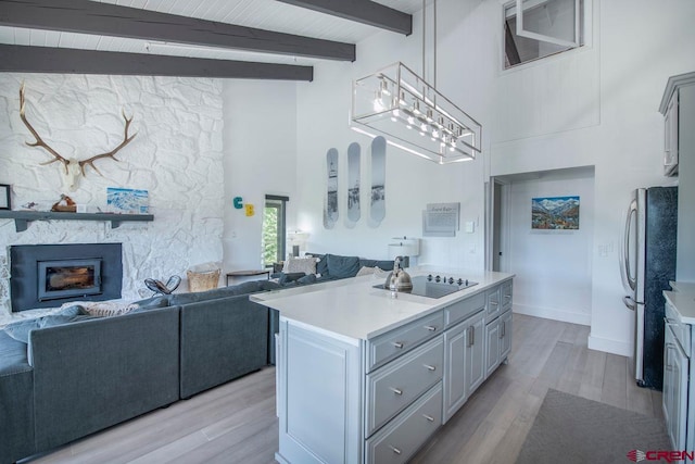 kitchen featuring light hardwood / wood-style flooring, black electric stovetop, a stone fireplace, stainless steel fridge, and beamed ceiling