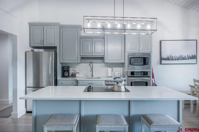 kitchen featuring stainless steel appliances, decorative light fixtures, light stone countertops, and sink