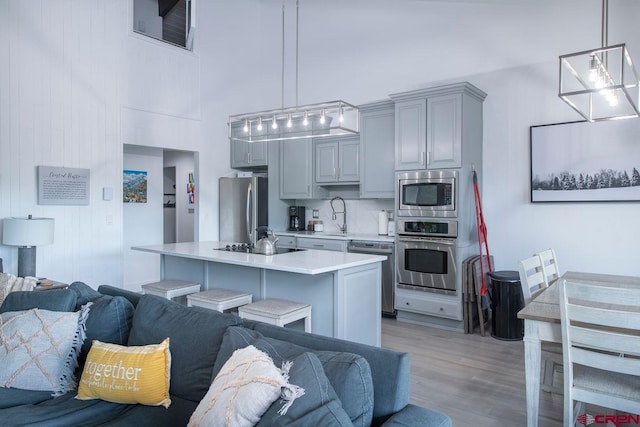 kitchen featuring a kitchen island, appliances with stainless steel finishes, a towering ceiling, decorative light fixtures, and gray cabinetry