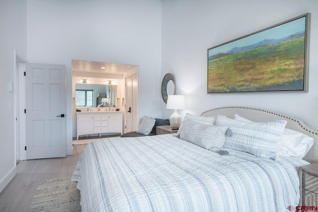 bedroom with connected bathroom, light hardwood / wood-style floors, and a high ceiling