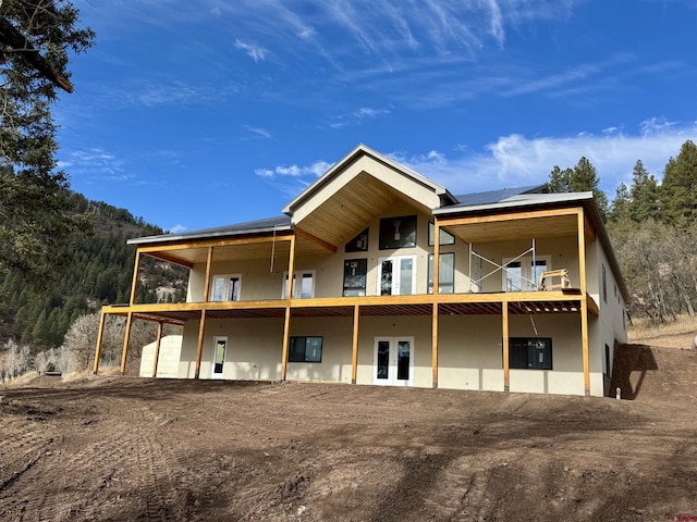 back of property with a balcony, stucco siding, solar panels, and french doors