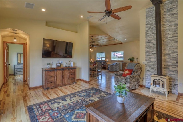 living room with ceiling fan, vaulted ceiling, a wood stove, and light wood-type flooring