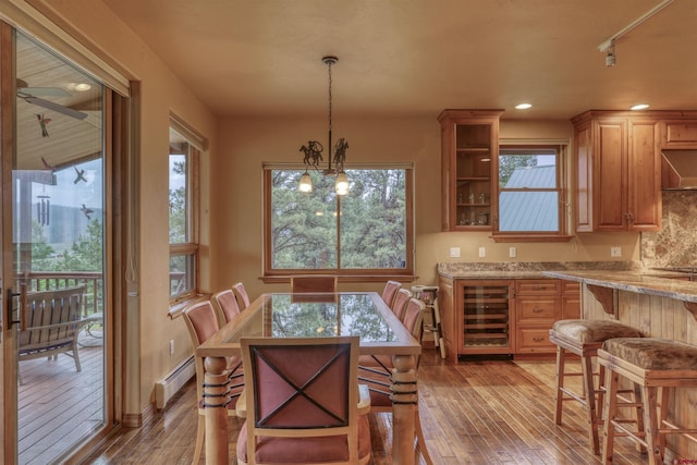 dining area with an inviting chandelier, wine cooler, a baseboard heating unit, wood-type flooring, and track lighting