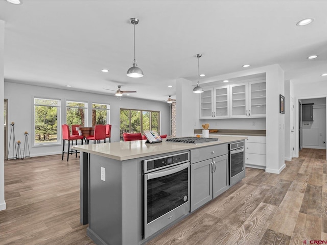 kitchen featuring light hardwood / wood-style floors, a kitchen island, ceiling fan, appliances with stainless steel finishes, and pendant lighting