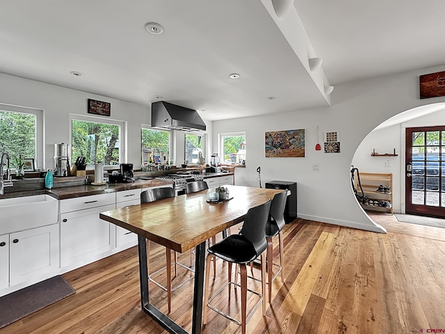 kitchen featuring white cabinetry, sink, wall chimney exhaust hood, a healthy amount of sunlight, and light hardwood / wood-style flooring