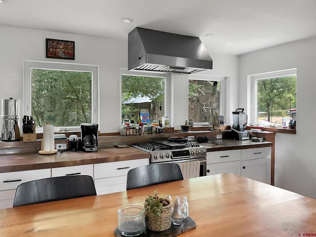 kitchen featuring high end range, white cabinetry, wall chimney exhaust hood, and wood counters