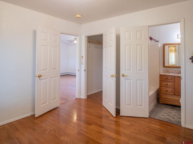 unfurnished bedroom with hardwood / wood-style floors, connected bathroom, a baseboard radiator, and a closet