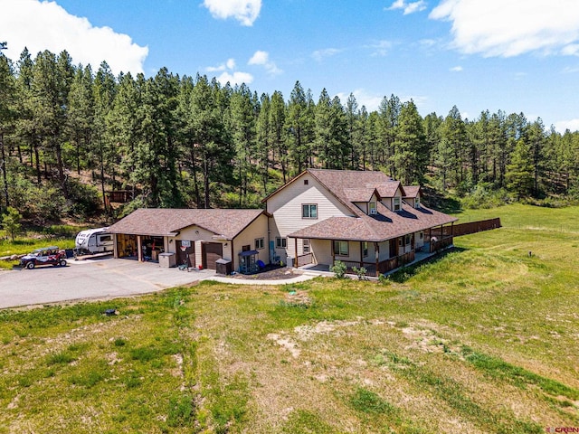 view of front of house featuring a front lawn, an attached garage, a forest view, and driveway