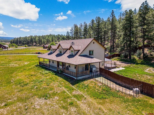 view of front of house featuring a front yard, fence, a wooded view, and roof with shingles