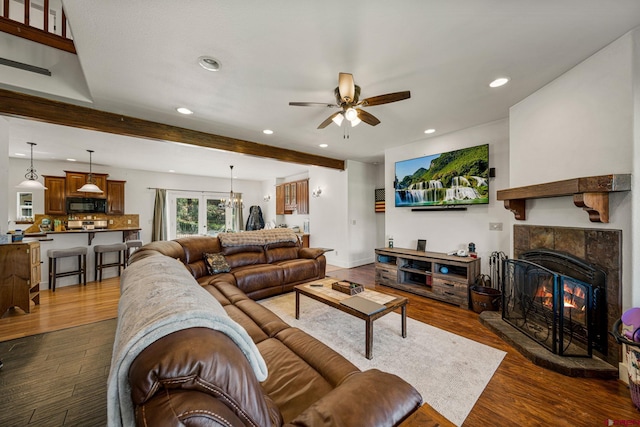 living room featuring a ceiling fan, beam ceiling, recessed lighting, a lit fireplace, and dark wood-type flooring