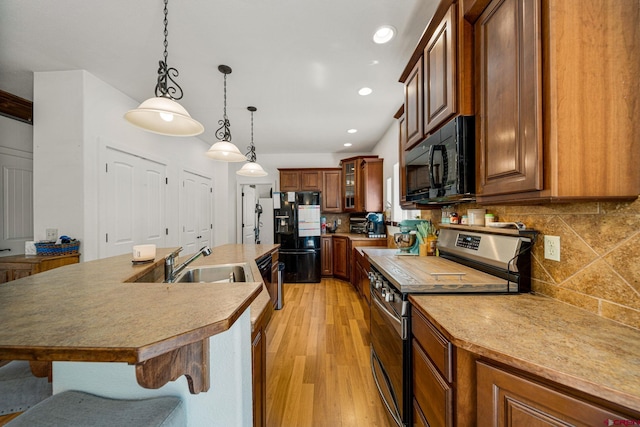 kitchen with light wood-type flooring, black appliances, a kitchen island with sink, decorative light fixtures, and decorative backsplash