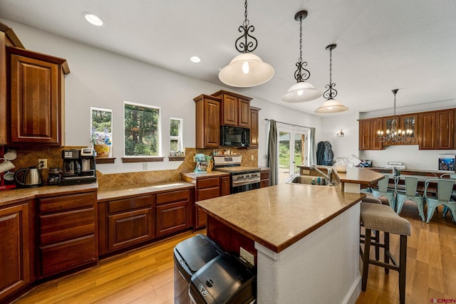 kitchen with a breakfast bar, black microwave, light wood finished floors, decorative backsplash, and gas range