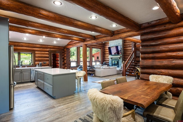 kitchen with rustic walls, beamed ceiling, a fireplace, a kitchen island, and light wood-type flooring