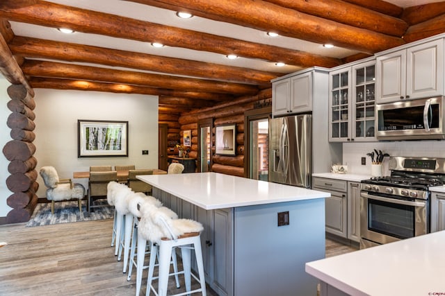 kitchen featuring decorative backsplash, appliances with stainless steel finishes, gray cabinetry, beamed ceiling, and a center island