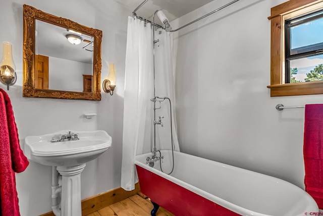 full bath with a shower with shower curtain, a freestanding bath, baseboards, and wood finished floors