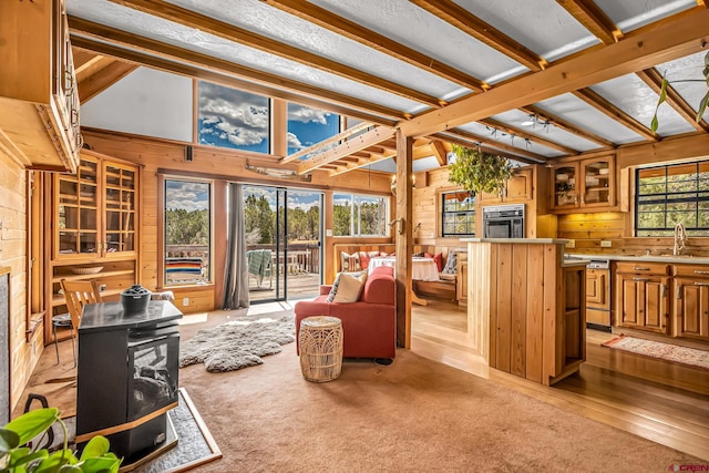 living room with beamed ceiling, wood walls, light wood-type flooring, and a wood stove