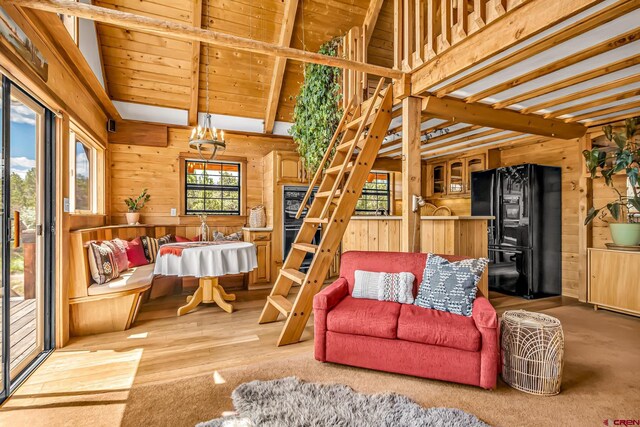 living room with wooden walls, lofted ceiling with beams, and light wood-type flooring