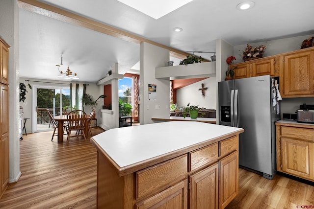 kitchen with stainless steel fridge, light wood-type flooring, a kitchen island, and a notable chandelier