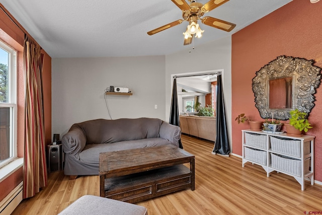 living room featuring ceiling fan, light wood-type flooring, and a baseboard heating unit