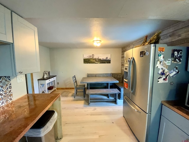 kitchen with dark countertops, stainless steel fridge, white cabinets, and light wood-style flooring