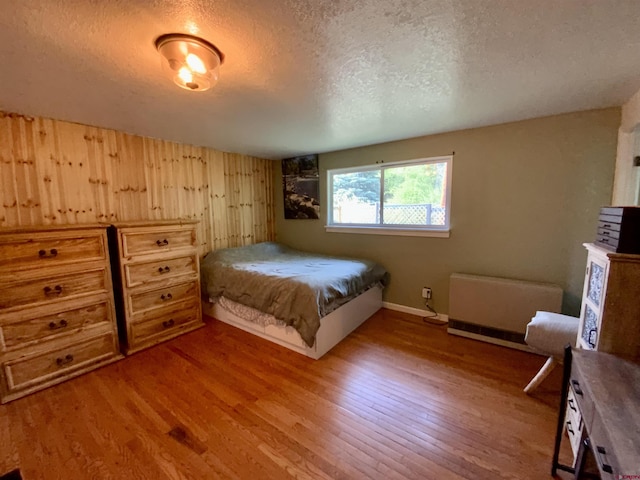 bedroom with radiator heating unit, a textured ceiling, and wood finished floors