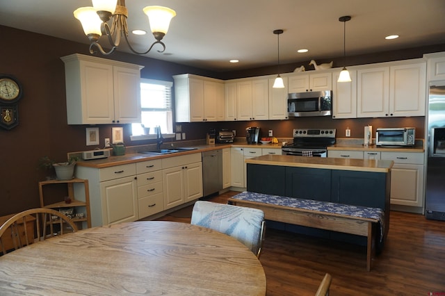 kitchen with appliances with stainless steel finishes, dark wood-type flooring, sink, white cabinets, and a chandelier