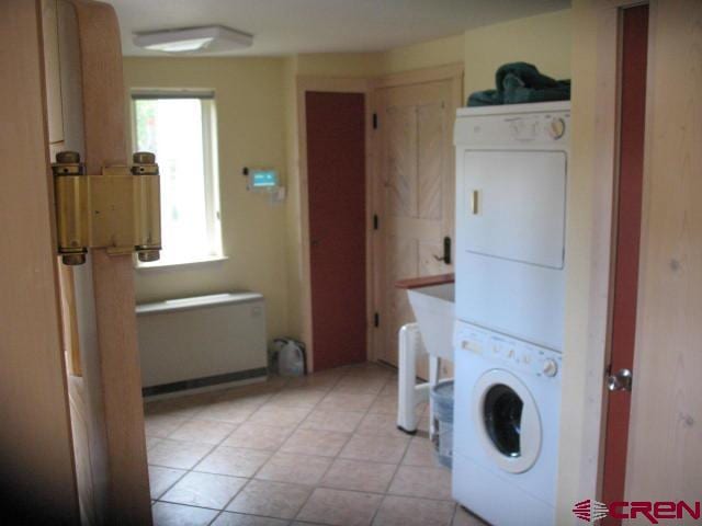 laundry area with stacked washer / dryer and light tile flooring