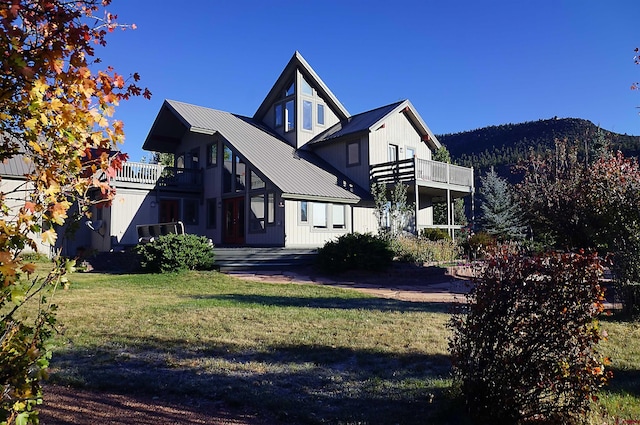 back of house with metal roof, a balcony, and a lawn