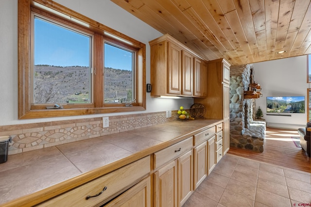 kitchen with wooden ceiling, a stone fireplace, tile countertops, and light hardwood / wood-style floors