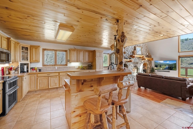 kitchen with appliances with stainless steel finishes, a fireplace, light tile floors, and light brown cabinets