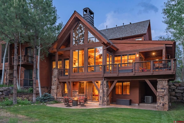 rear view of property featuring central AC, a patio area, a lawn, and an outdoor fire pit