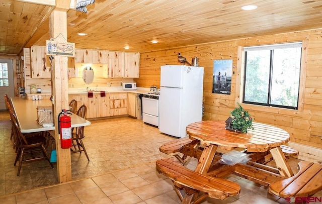 kitchen featuring light brown cabinets, wooden walls, white appliances, and light tile patterned floors