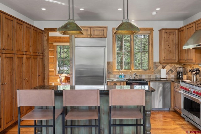 kitchen featuring premium appliances, light hardwood / wood-style flooring, dark stone counters, decorative backsplash, and decorative light fixtures