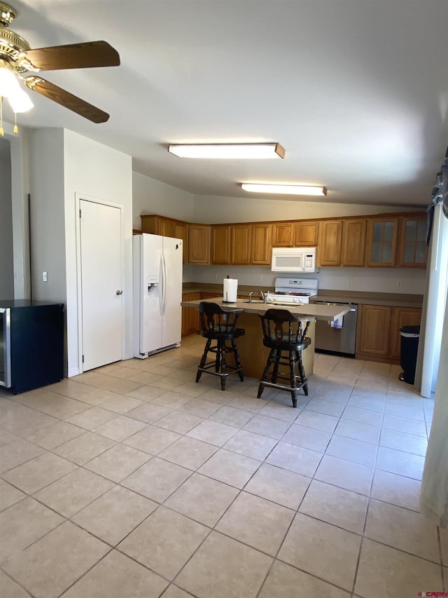 kitchen with light tile patterned flooring, a breakfast bar area, ceiling fan, white appliances, and a kitchen island with sink