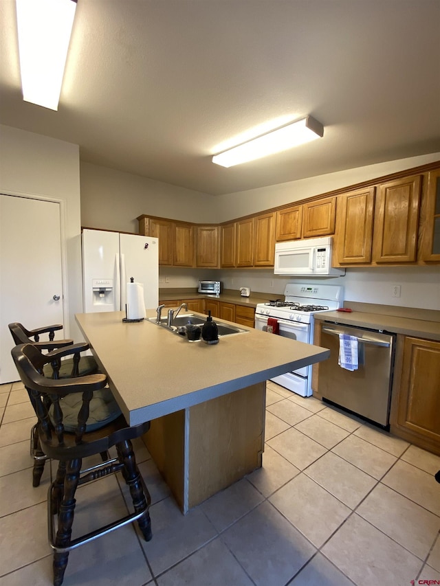 kitchen with light tile patterned flooring, a breakfast bar, sink, an island with sink, and white appliances